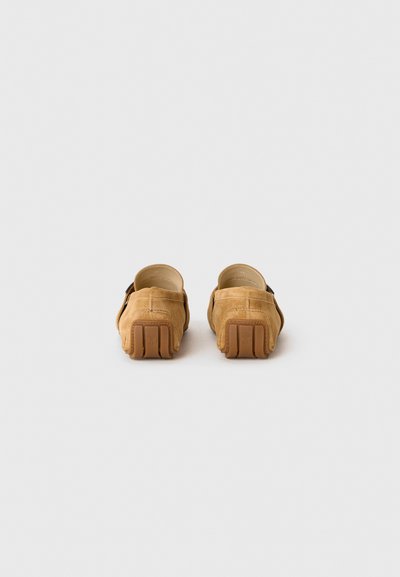 Pantofi slip-on din suede bej, cu o formă rotundă, căptușiți cu piele fină și cu o talpă din cauciuc texturată. Detalii minore de cusătură vizibile.