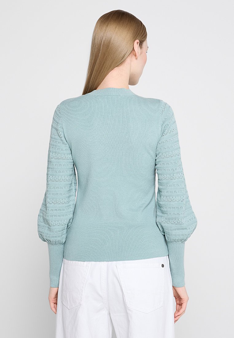Lichtblauwe gebreide trui met textuurpofmouwen en geribde manchetten. Beschikt over een klassieke ronde halslijn en een getailleerde pasvorm.