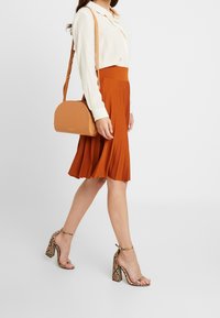 Krémová blůza v kombinaci s oranžovou skládací sukní, doplněná světlou krosnou taškou a lodičkami s hadím vzorem.
