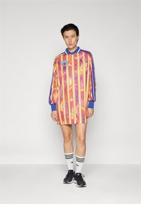 Long-sleeve shirt dress with pink and orange vertical stripes, blue collar, and logo patch, paired with black shoes and white striped socks.