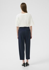 T-shirt blanc oversized avec une coupe décontractée, associé à un pantalon navy à jambes fuselées et deux poches arrière. Chaussures à talons noires.
