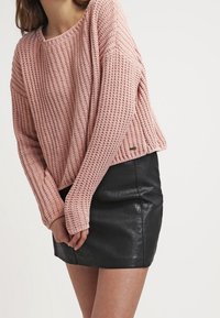 Rosa strickpullover mit lockerer Passform und weitem Ausschnitt, kombiniert mit einem schwarzen Leder-Minirock, der eine gerippte Textur und Saumdetails aufweist.