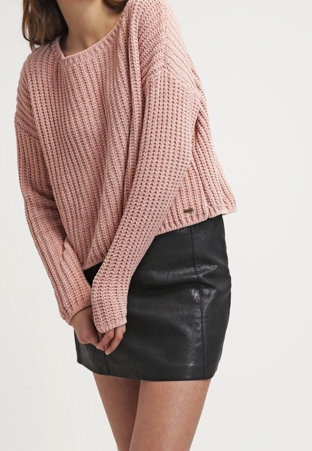 Rosa strickpullover mit lockerer Passform und weitem Ausschnitt, kombiniert mit einem schwarzen Leder-Minirock, der eine gerippte Textur und Saumdetails aufweist.