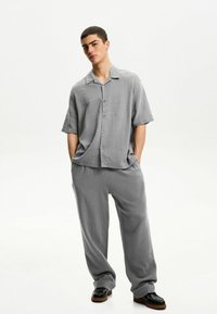 Gray short-sleeve button-up shirt with a textured finish, paired with loose-fitting gray pants. Worn with black shoes.