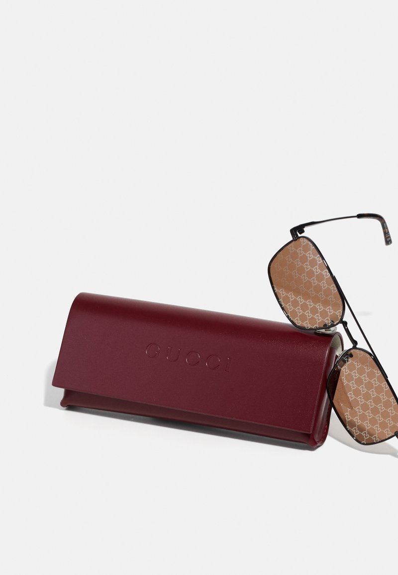 Custodia per occhiali da sole in pelle bordeaux con logo "GUCCI" in rilievo. Occhiali da sole in metallo grigio con lenti marroni e motivo logo ripetuto.