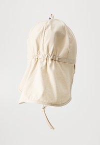 Chapeau en coton beige avec une couronne froncée, un bord allongé et une sangle ajustable sous le menton ; possède une texture lisse et de simples détails de couture.