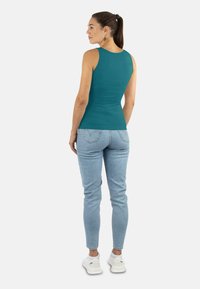 Türkises ärmelloses Oberteil mit tailliertem Design, kombiniert mit hellblauen Jeans und weißen Sneakers. Glatter Stoff und klare Linien.