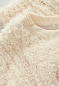 Cremefarvet fleece sweater med en tekstureret, plysset overflade og ribbet halsudskæring, der fremhæver et blødt og varmt stof.