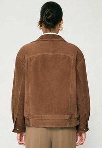 Brun mockakav jacket med klassisk krage, avslappnad passform och tryckknappsmanschetter, med en mjuk textur och minimalistisk design.