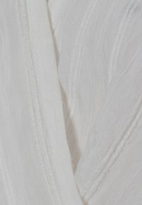 Gros plan d’un tissu blanc avec des rayures texturées verticales et des détails de tissage visibles.