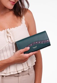 Green leather wallet with a curved design, featuring a multicolored polka dot band. Gold logo on the front. Smooth texture.