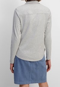 Gray long-sleeve shirt with a collar, featuring a smooth texture. Paired with a blue corduroy skirt, visible seam and hem details.