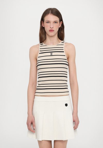 Débardeur rayé beige et noir, texture côtelée, avec un design ajusté et un logo au centre; associé à une jupe plissée blanche avec un accent noir.