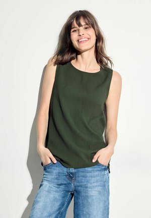 Haut sans manches vert foncé avec une finition texturée, encolure ronde, associé à un jean en denim bleu clair, mannequin se tenant devant un fond uni.