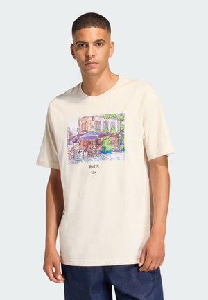 Lichtbeige katoenen T-shirt met een kleurrijke illustratie van een Parijse café en tekst. Korte mouwen, ronde hals, relaxte pasvorm.