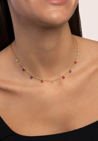 Collana in oro con più pietre preziose colorate (rosse, viola, trasparenti) sospese a intervalli, che accentuano il collo.