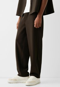 Bruna vida byxor i ett texturerat material, med en avslappnad passform och kombinerade med off-white sneakers.