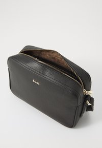 Pochette da toilette in pelle nera con superficie testurizzata, chiusura con zip dorata e fodera interna di una tonalità marrone più chiara. Presenta un piccolo logo.