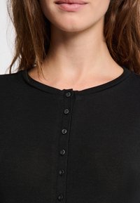 Haut noir côtelé avec un col arrondi, présentant une patte de boutonnage sur le devant et une texture subtile dans le tissu.