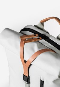 Weißer Rolltop-Rucksack mit Lederträgern, einem schwarzen Reißverschluss und einer Seitentasche. Glatte Textur mit kontrastierenden Brauntönen und grauen Akzenten.