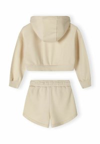Sudadera corta de color crema con capucha y puños acanalados, combinada con pantalones cortos con cordón a juego, que cuentan con una textura suave y un ajuste relajado.