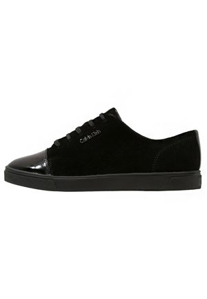 Zapatilla baja negra con cuerpo de ante, puntera de cuero charol, cordones negros y logo de Calvin Klein en el lateral.