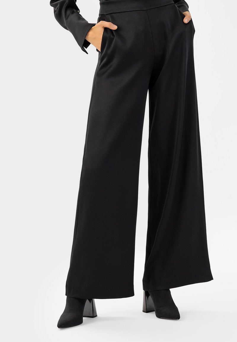 Zwarte wijde broek gemaakt van soepel materiaal, met zijzakken en een hoge taille. Gepaard met zwarte hoge enkellaarsjes.