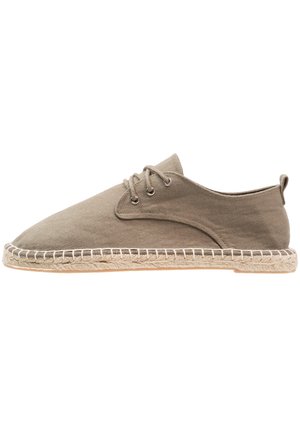 Casual lage veterschoen in beige canvas met espadrille-achtig ontwerp, jute-omhulde zool en witte stikselaccenten.