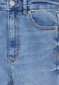 Tela de mezclilla azul con una ligera textura desgastada, con costuras de cobre, un bolsillo frontal y un cierre de botón en la cinturilla.