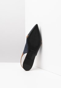 Spidskåret sko med et denim-overdel, sort tekstureret sål og en brun rem. Designet har en slank silhuet og minimal hardware.