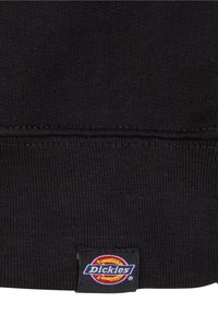Svart strikket genserstoff med ribbestruktur. Har en sydd Dickies logo-lapp i rødt, gult og blått nederst.