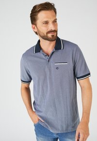 Polo blu navy realizzato in tessuto a trama con strisce bianche di accento sul colletto e sulle maniche, dotato di taschino sul petto.