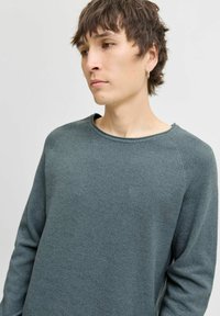 Pulover texturat gri cu decolteu rotund și mâneci raglan. Prezintă un model de tricot subtil și o croială lejeră.
