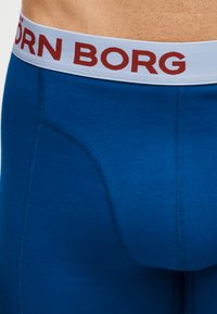 Μπλε ανδρικά εσώρουχα boxer με λευκή μέση που φέρει κόκκινο κείμενο "BJÖRN BORG", φορεμένα σε γυμνό κορμό.