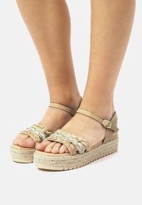 Sandalias de plataforma marrones con correas tejidas multicolores y un broche en el tobillo. Presenta una suela envuelta en yute y un fondo texturizado para mayor agarre.