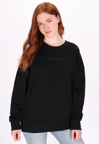 Felpa nera oversize realizzata in tessuto morbido, con collo a girocollo e polsini a costine, con un discreto dettaglio testuale sul davanti.