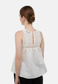 Blouse sans manches blanche avec un dos en dentelle texturée, une ouverture en forme de clé et une coupe ample. Fabriquée en tissu léger.