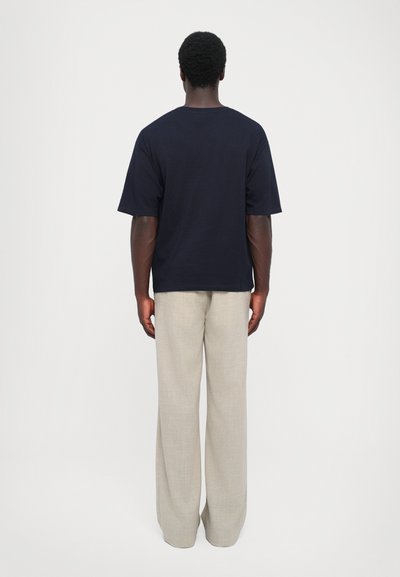 Ναυτικό βαμβακερό t-shirt με κοντά μανίκια, συνδυασμένο με ελαφριά μπεζ λινά παντελόνια. Απλός σχεδιασμός χωρίς ορατά σχέδια ή λογότυπα.