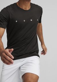Černé sportovní tričko s krátkým rukávem, se bílým logem "PUMA" na hrudi. Vyrobeno z hladkého, lehkého materiálu.
