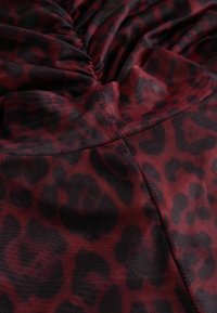 Czerwono-czarna tkanina w wzór panterki o strukturalnym wykończeniu; charakteryzuje się marszczeniami, które tworzą delikatne fałdy i gładki design.