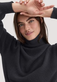 Dunkelgrauer Rollkragenpullover mit lockerer Passform, weichem Material und gerippten Details am Kragen und an den Bündchen. Nahaufnahme-Porträt.