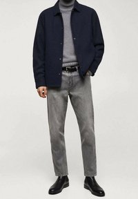Navy button-up jacket over a gray turtleneck, paired with light gray jeans and black ankle boots. Casual, structured fit.