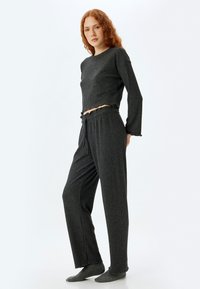 Harmaa ribbattu loungewear-setti, jossa pitkät hihat, lyhyt paita ja joustavat housut. Mukana rypytyshelma ja pehmeä kangas.