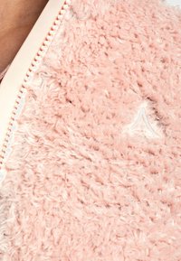 Różowa, puszysta kurtka z miękkim, teksturowanym wykończeniem. Posiada jasny zamek błyskawiczny oraz małe, haftowane logo na tkaninie.