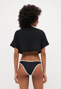 T-shirt nera corta con maniche corte e vestibilità rilassata, abbinata a perizoma nero con rifiniture bianche. Tessuto morbido.