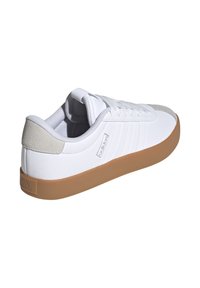 Scarpa sportiva bianca con una tomaia testurizzata, dettagli grigi e una suola in gomma marrone. Caratteristiche includono chiusura con lacci e logo ai lati.