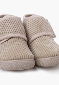 Beige corduroy slippers met een zachte textuur, voorzien van een klittenbandsluiting en een gevulkaniseerde rubberen zool voor grip en stabiliteit.