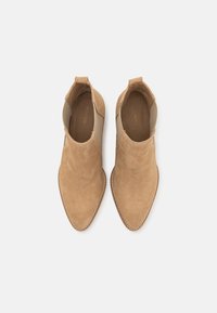 Tan daimové kotníkové boty s špičatou špičkou, elastickými bočními panely a prošíváním kolem okraje. Hladká struktura a minimalistický design.