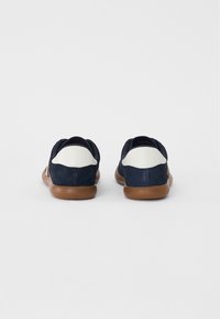 Tamsiai mėlyni zomšiniai bateliai su baltais odiniais akcentais ant kulno, turi lanksčią rudą gumos padą ir apvalią formą.