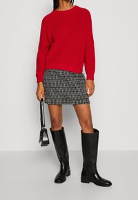 Maglione rosso a coste abbinato a una minigonna a fantasia bianco e nero. Gli stivali neri in pelle al ginocchio e una piccola borsa nera completano il look.